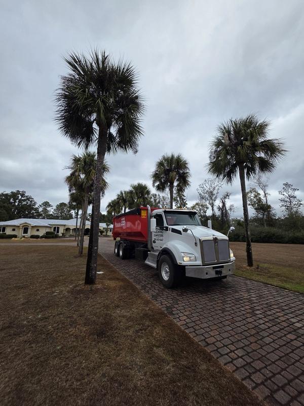 Muckpro roll-off truck delivering a dumpster on a palm-lined residential driveway in Perry FL